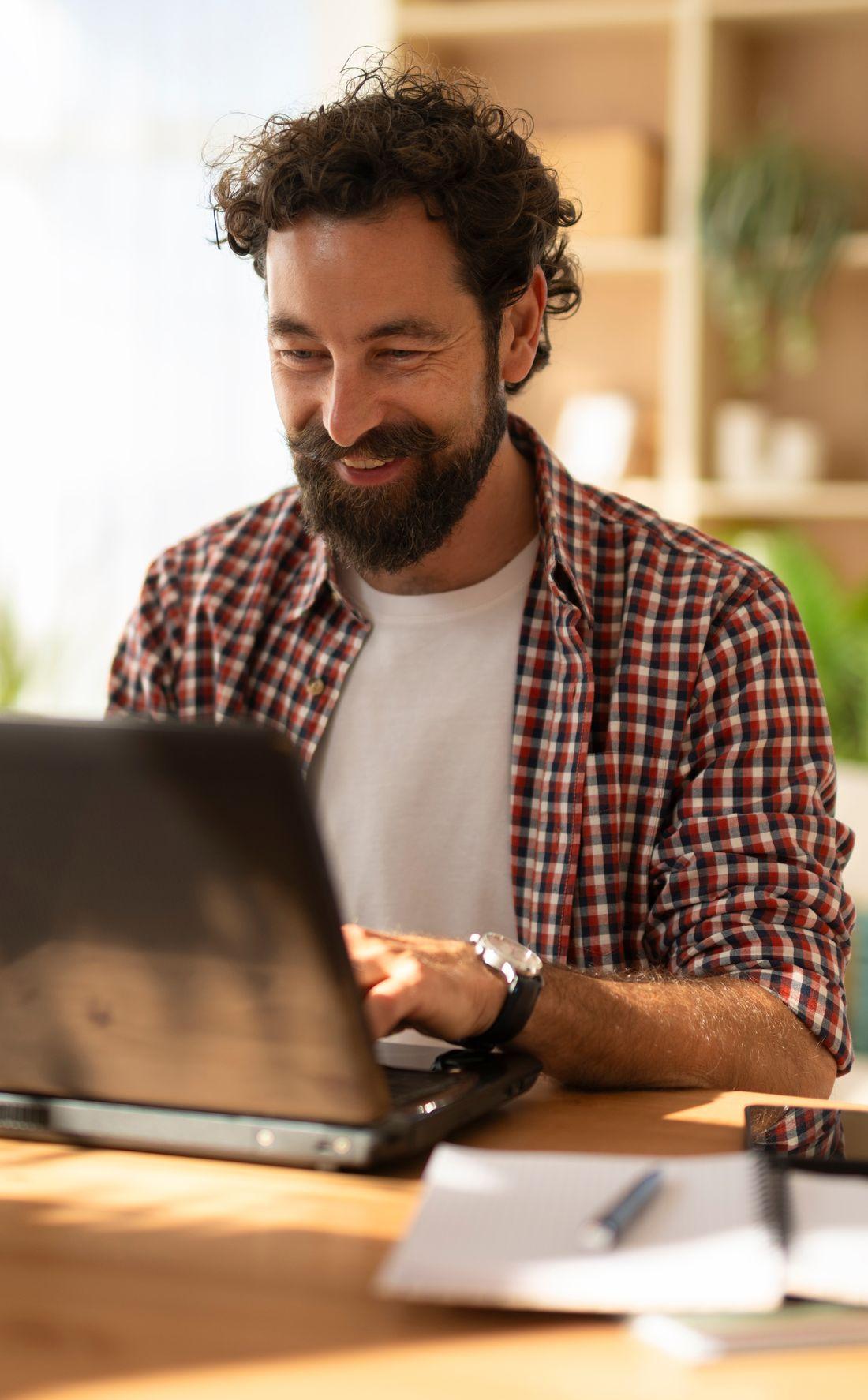 A business owner smiling at his laptop at a kitchen table