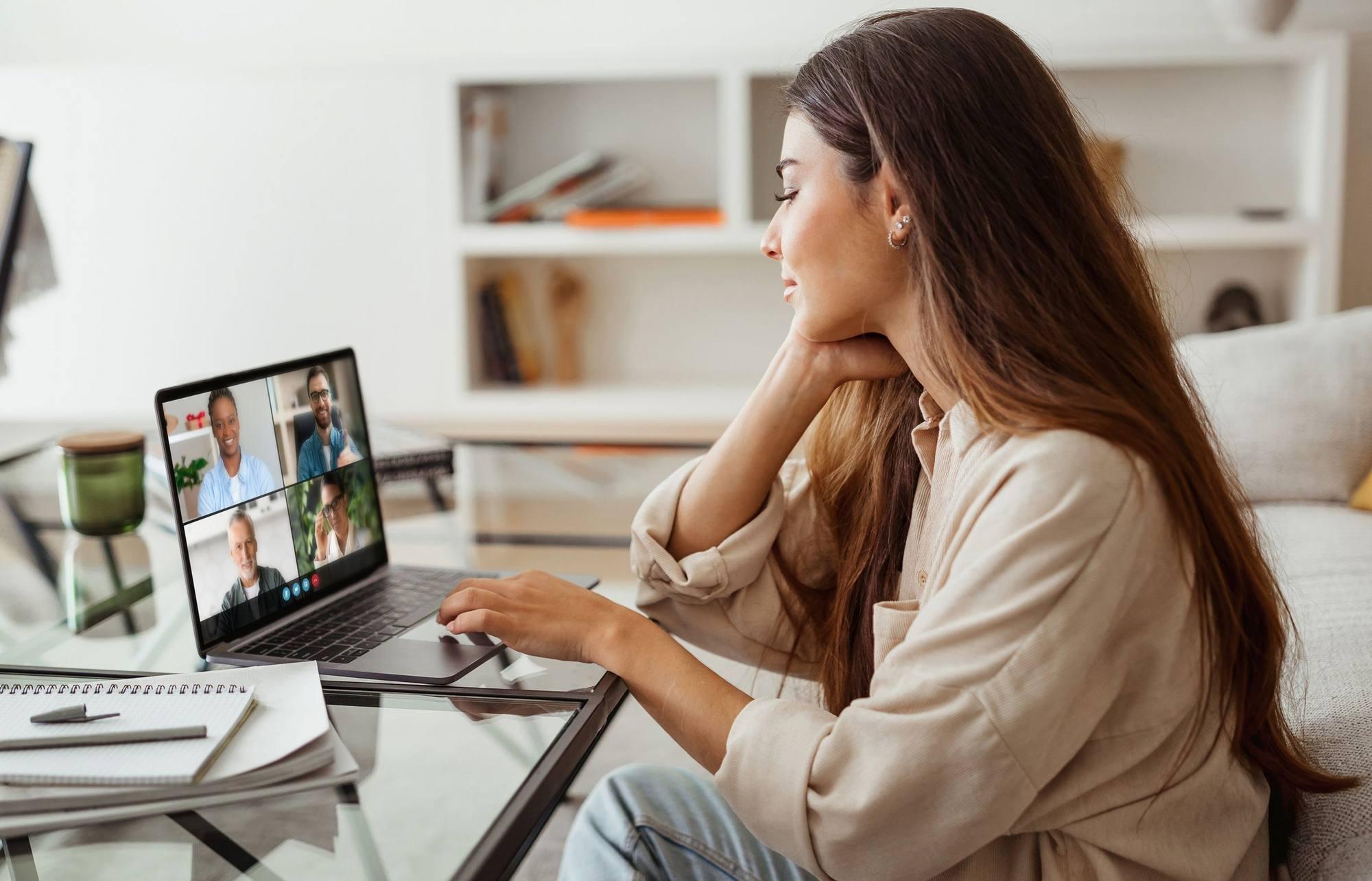 A woman at home on a video call, faces on her laptop screen