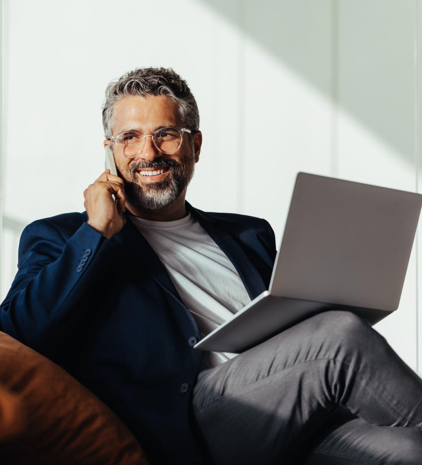 An experienced man on a phone call, laptop on his knee