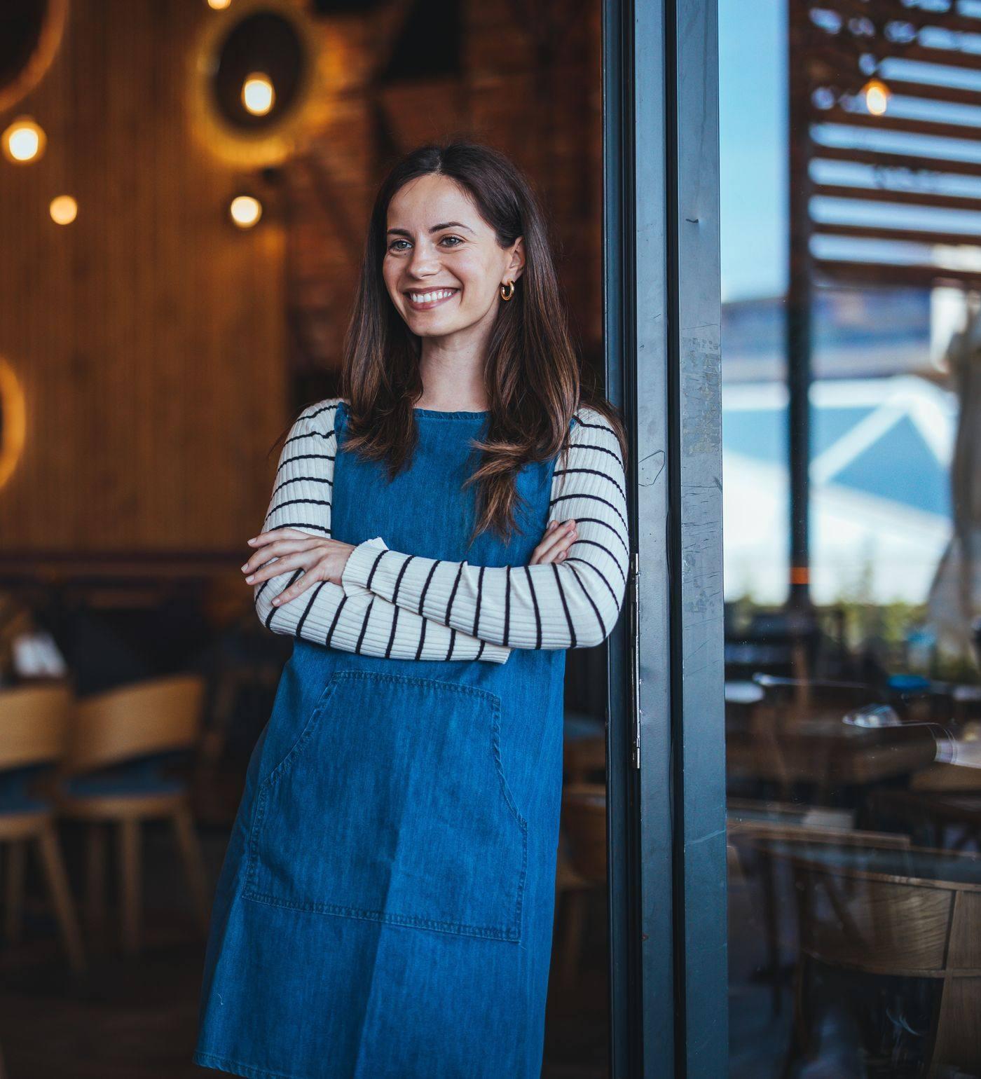A café owner in an apron standing in the doorway of her restaurant
